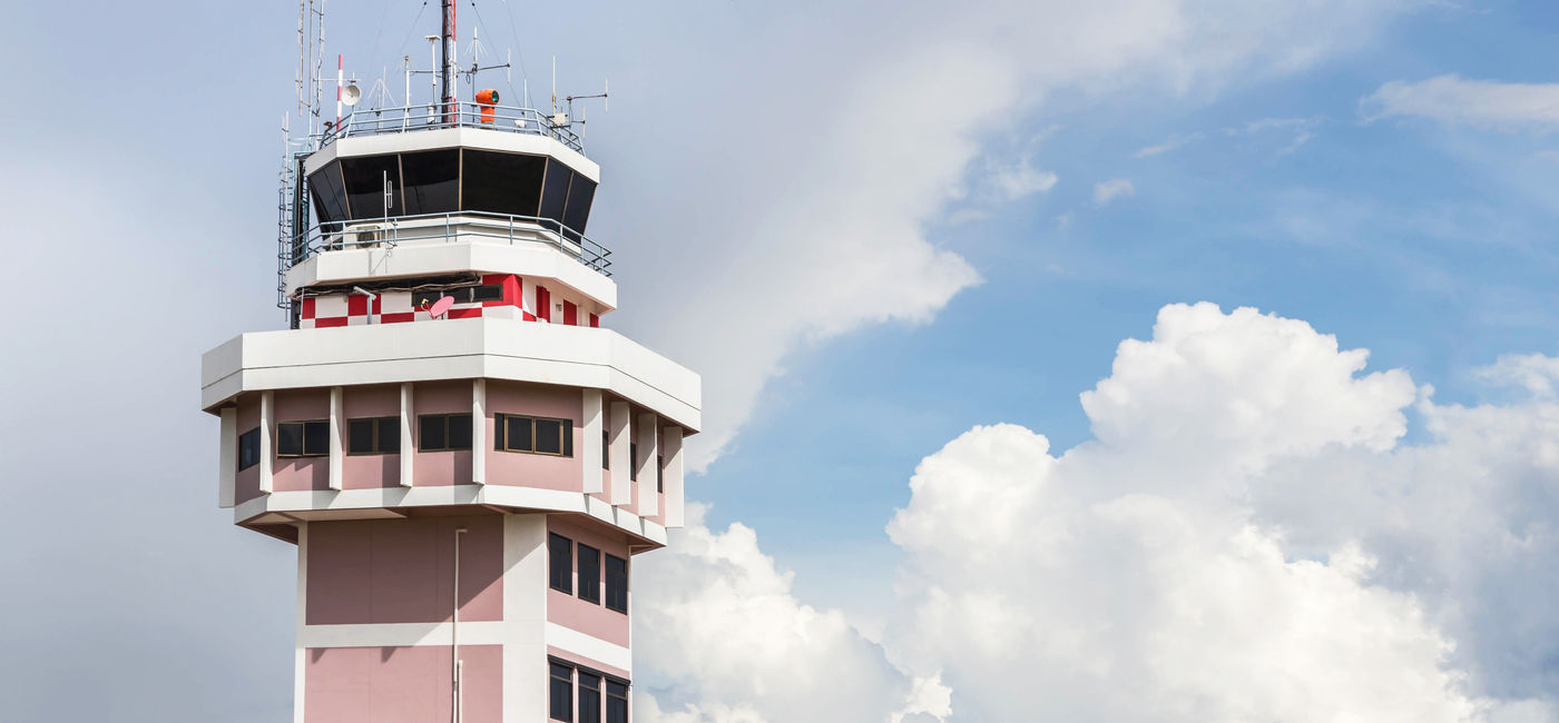 Image: Air traffic control tower with an airplane taking off in the foreground. (Photo Credit: Adobe Stock/Soonthorn)