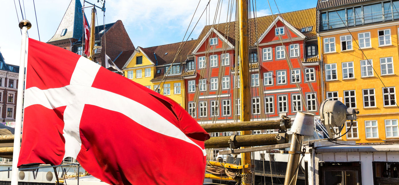 Image: Denmark's national flag flying in the foreground of Copenhagen's famous old Nyhavn port. (photo via iStock/Getty Images Plus/nantonov)