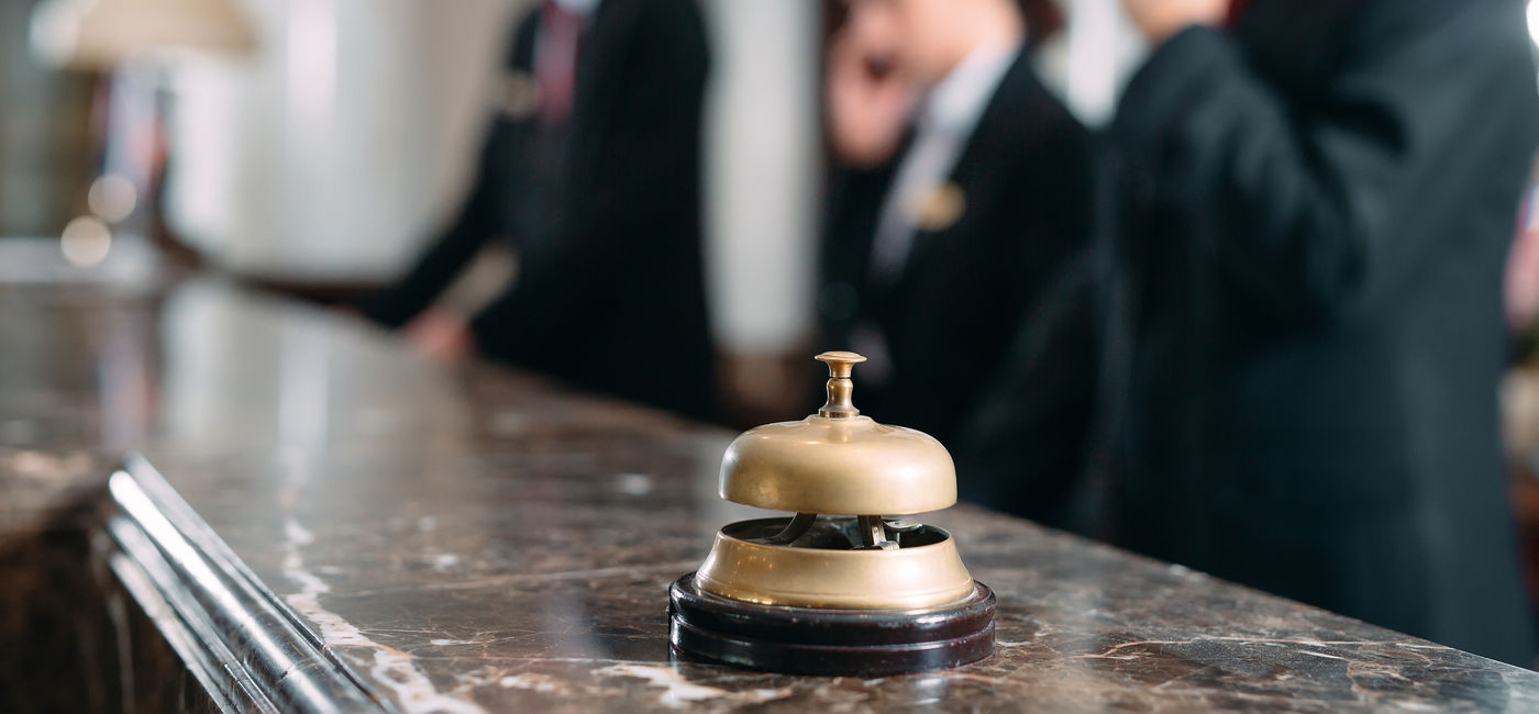 Image: Hotel staff working at reception counter with service bell. (Photo Credit: Adobe Stock/davit85)