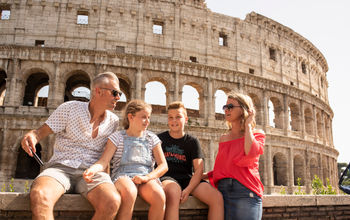 A family of travelers sits in front of the Colosseum in Rome, Italy.