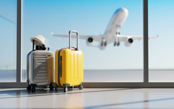 Luggage sitting at the airport with a plane taking off in the background.